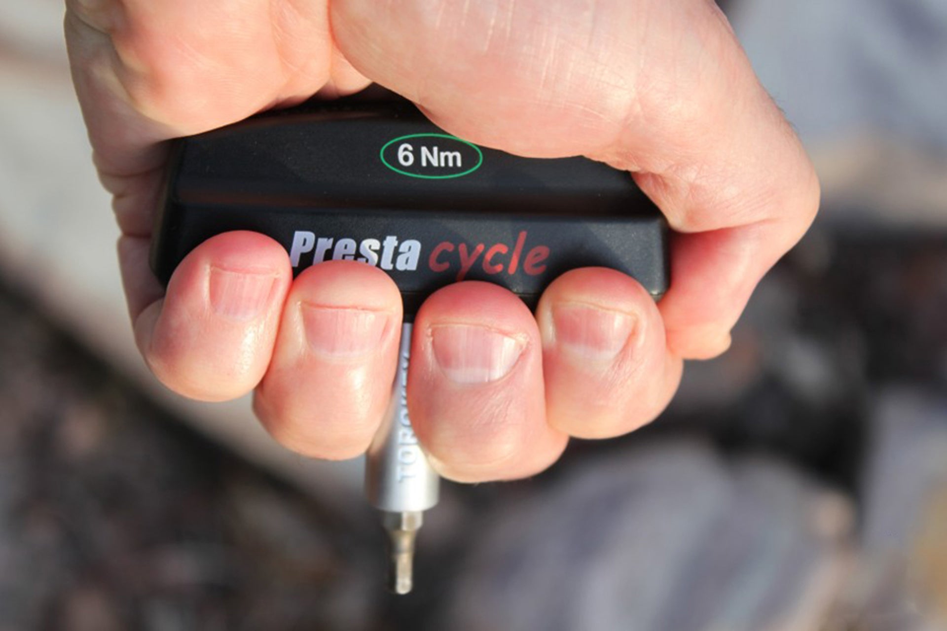 A close-up of a hand holding a Prestacycle Pro TorqKeys 5Nm T-Handle Torque-Limiting Bits Tool, with the 5Nm label visible on top and the tool’s metal tip pointing downward.