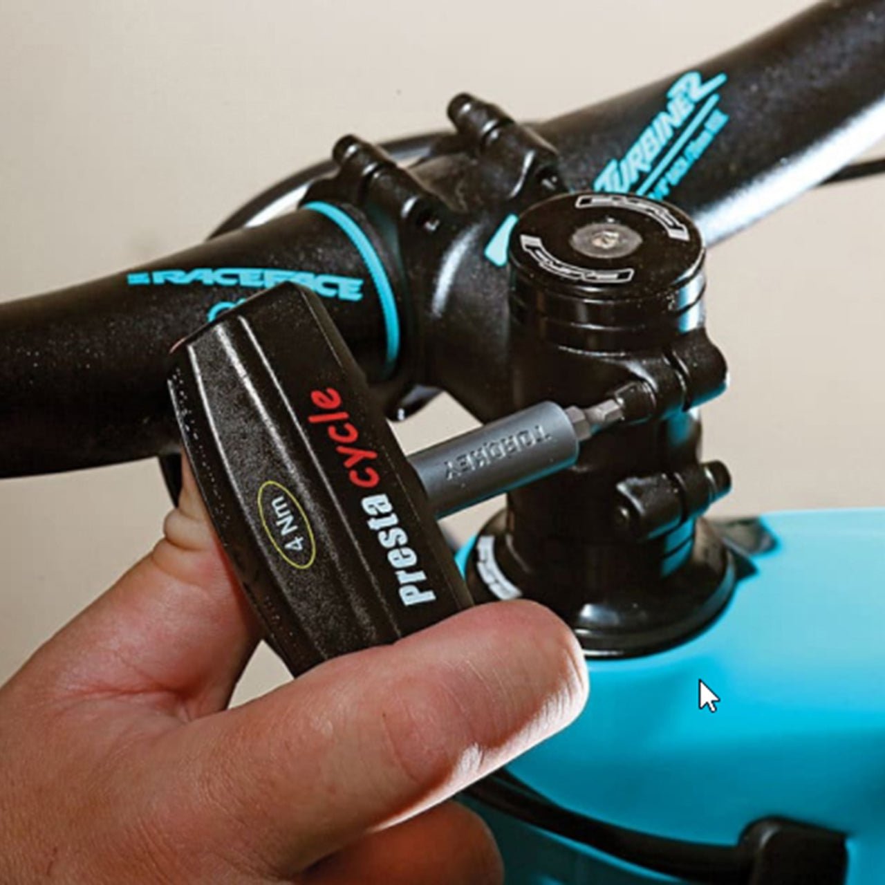 A hand uses a Prestacycle Pro TorqKeys 5Nm T-Handle Torque-Limiting Bits Tool to tighten a bolt on a bicycle’s handlebar stem, with Race Face branding visible on the handlebars.