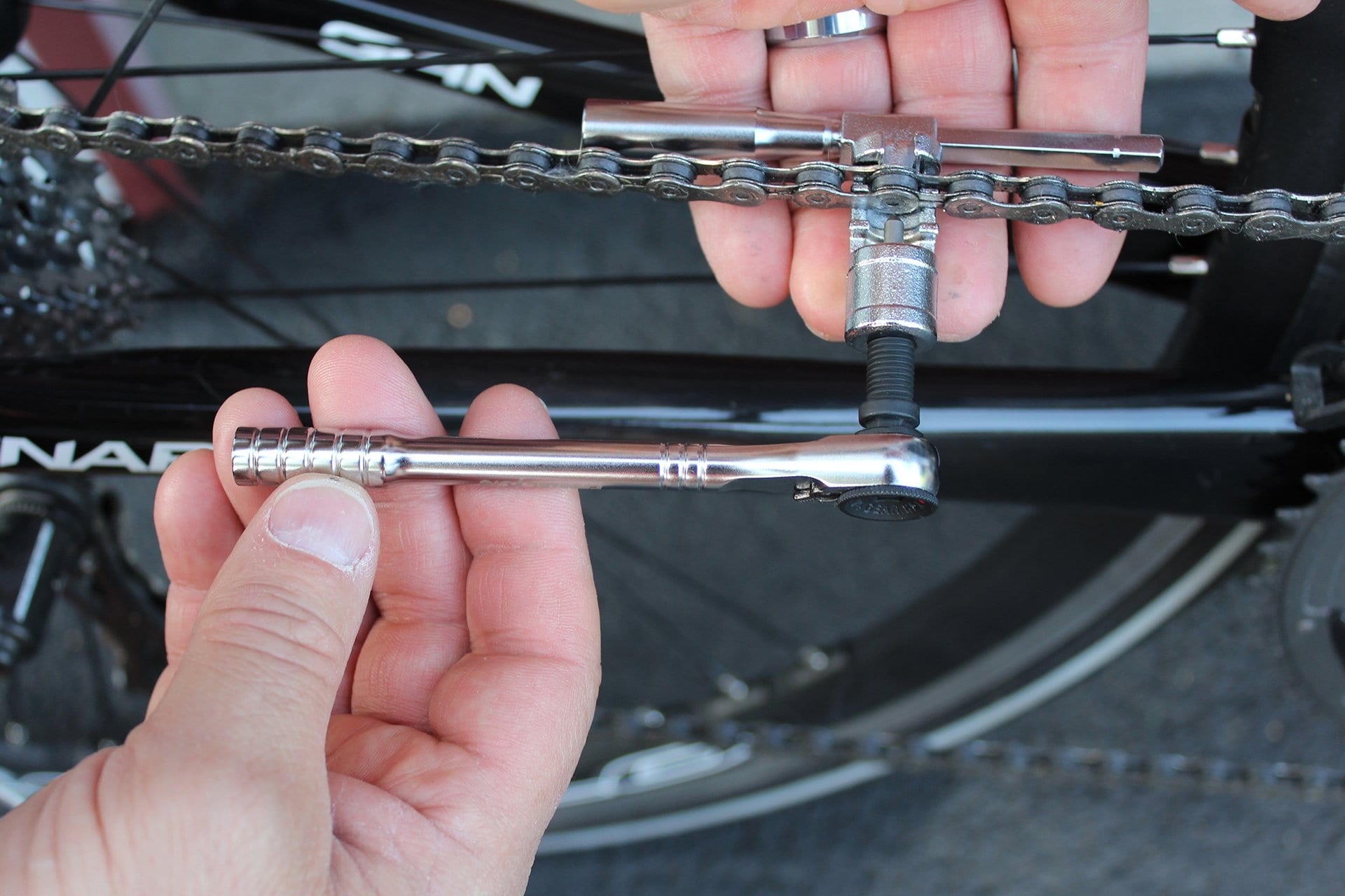 Using the Prestacycle PrestaRatchet Chain Accessory, a person can repair or adjust a bike chain by positioning the tool on a chain link above the frame and operating it with a ratchet wrench.