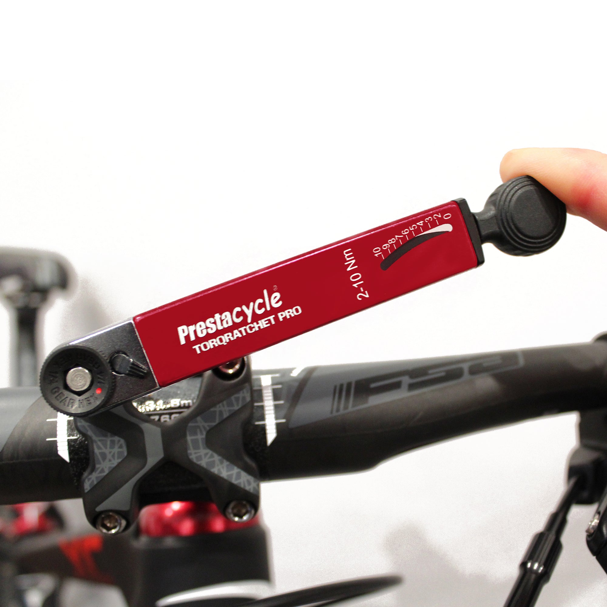 A hand uses the Prestacycle TorqRatchet PRO Deluxe, a reversible multi-tool and 2~10Nm torque ratchet, to adjust bolts on a black bicycle stem and handlebars.