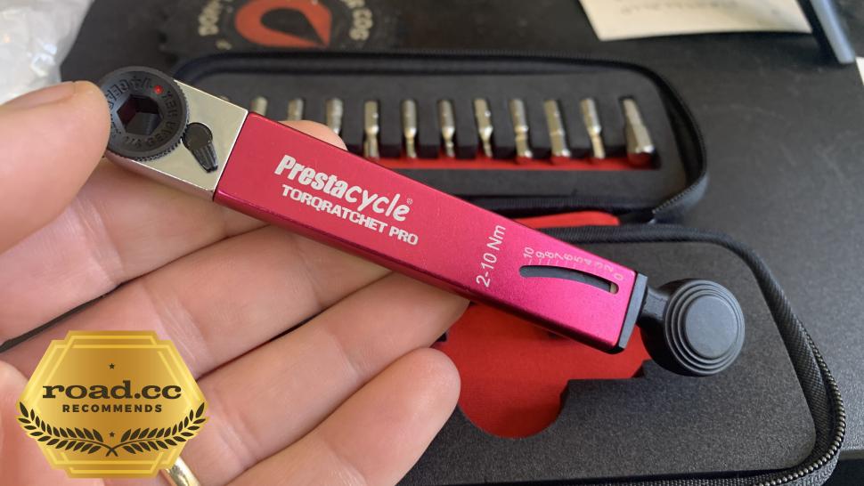 A red Prestacycle TorqRatchet PRO Deluxe (2–10Nm) Pro Pocket Multi-tool is shown close-up with bits in a black case behind it. A gold road.cc recommends badge appears in the lower left corner of the image.