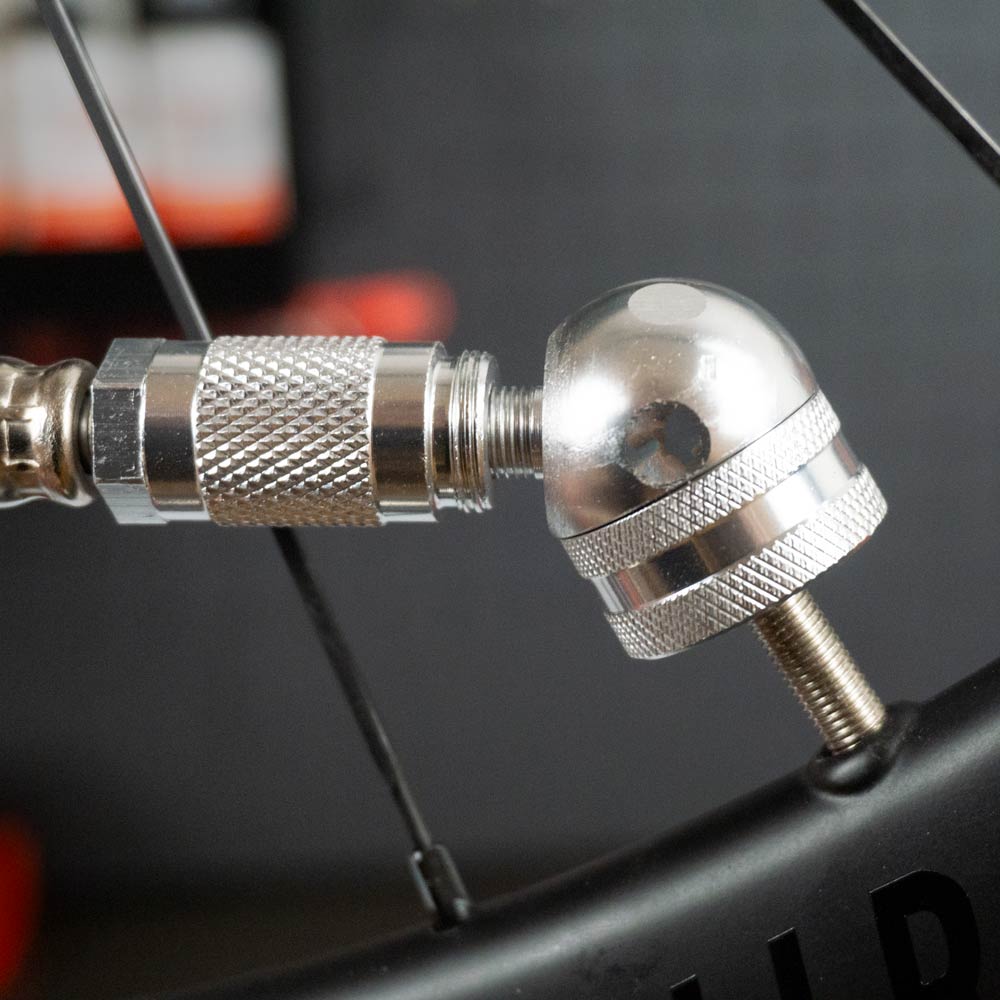 Close-up of the Prestacycle Big Angle Presta Head by Prestacycle attached to a bicycle valve, showcasing its detailed metallic design and ideal fit for tubeless tire applications against a blurred background.