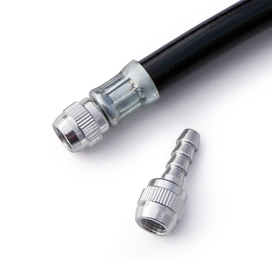 A close-up of a Prestacycle Schrader Hose Barb, featuring a black hose with a metal connector attached and an additional metal connector beside it, displayed on a white background.