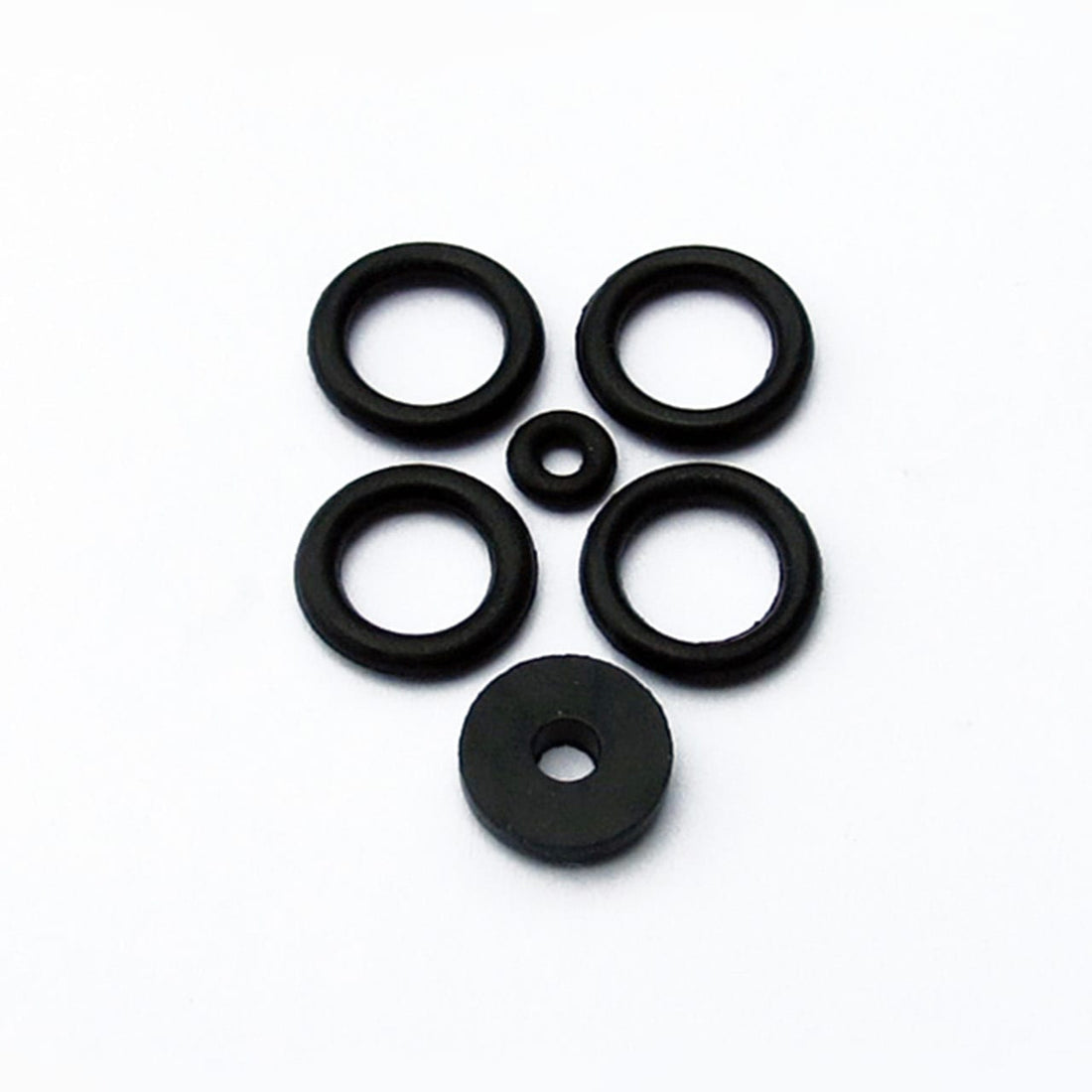 Five black o-rings and one washer from the Prestacycle Prestaflator Rebuild Kit are arranged on a white surface to resemble a simple face, with the washer as the mouth and the smallest o-ring as the nose.