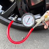 A person uses the Prestacycle Prestaflator PRO Bicycle Tire Inflator with Presta & Schrader compatibility to check air pressure on a car’s black tire, parked on gray pavement.