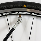 A black pump with the Prestacycle Angle Mini Presta Head attached to a Continental Grand Prix 4 Season tubeless tire, mounted on a black and silver rim.