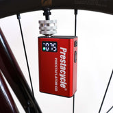 A red Prestacycle Prestaflator GO Portable Digital Rechargeable Preset Bicycle Tire Inflator, perfect for electric bikes, is connected to a bicycle wheel and shows the pressure reading on its display.