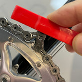 A hand uses the Prestacycle Prestalever GO 5-in-1 Multi-tool Tire Lever near a bicycles gears, possibly to check chain alignment or wear.