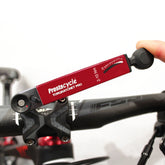 A hand uses the Prestacycle TorqRatchet PRO Deluxe, a reversible multi-tool and 2~10Nm torque ratchet, to adjust bolts on a black bicycle stem and handlebars.