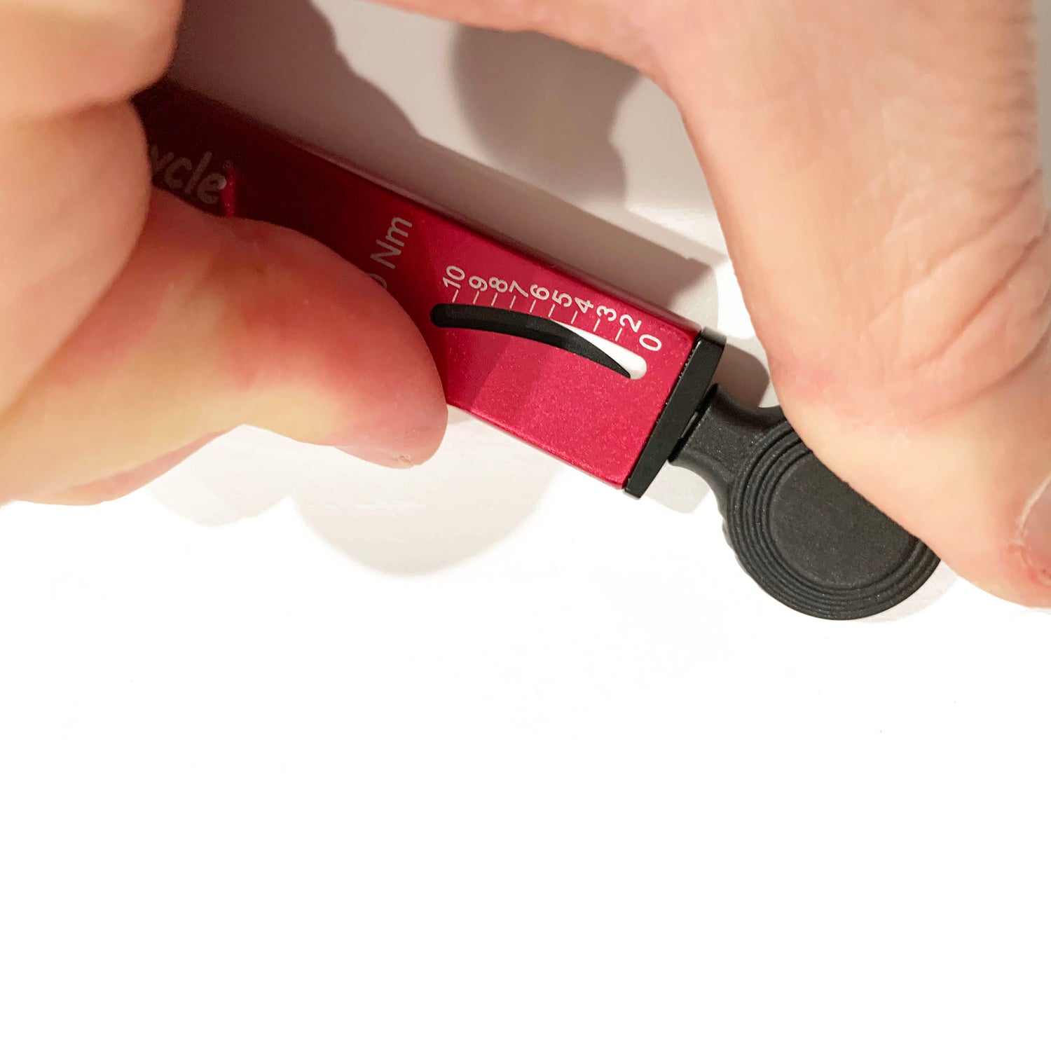 A close-up of a hand adjusting the Prestacycle TorqRatchet PRO Wallet, a red multi-tool torque ratchet (2–10Nm), with visible measurement markings.