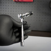 A hand in a black glove holds the Prestacycle Bits Swivel QR Torque Wrench Adapter by Prestacycle, a shiny metal tool with socket attachment, against a dark perforated background.