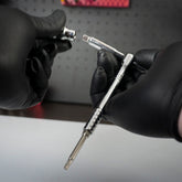 A person wearing black gloves holds a Prestacycle Bits Swivel QR Torque Wrench Adapter in one hand and a compatible socket in the other, ready to attach it. The background is blurred.