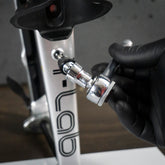 A gloved hand uses a Prestacycle Bits Swivel QR Torque Wrench Adapter to adjust a bolt on a metallic frame labeled LAB, suggesting bicycle maintenance or assembly.