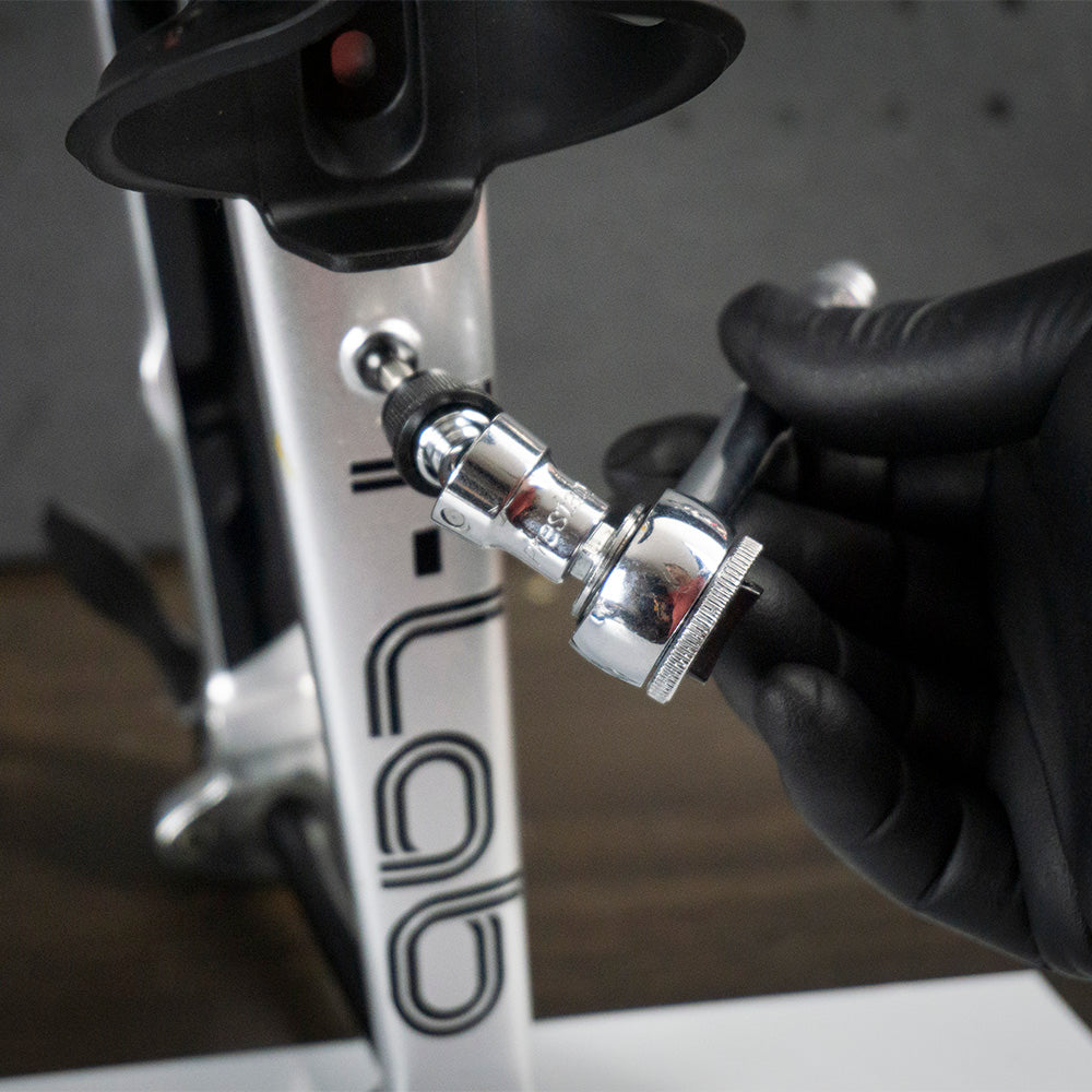 A gloved hand uses a Prestacycle Bits Swivel QR Torque Wrench Adapter to adjust a bolt on a metallic frame labeled LAB, suggesting bicycle maintenance or assembly.