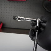 A gloved hand holds the Prestacycle Bits Swivel QR Torque Wrench Adapter by Prestacycle—an essential tool for use with torque wrenches—against a black pegboard backdrop.
