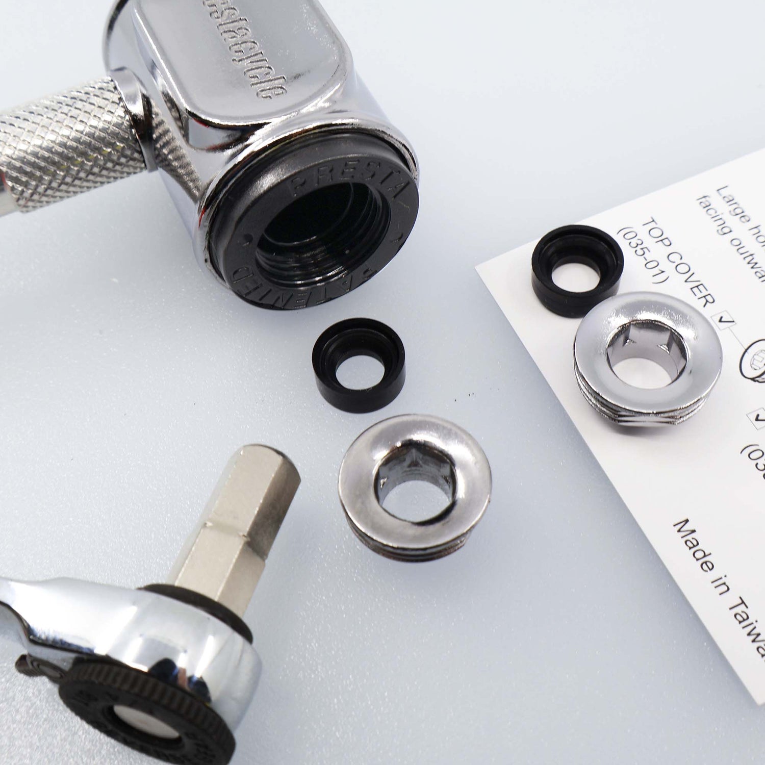 A close-up of a Prestacycle Prestaflator Pro Presta Head Rebuild Kit shows the ratchet tool, metal washers, black rubber rings, and paper manual on a light surface, highlighting the components for assembly or repair.