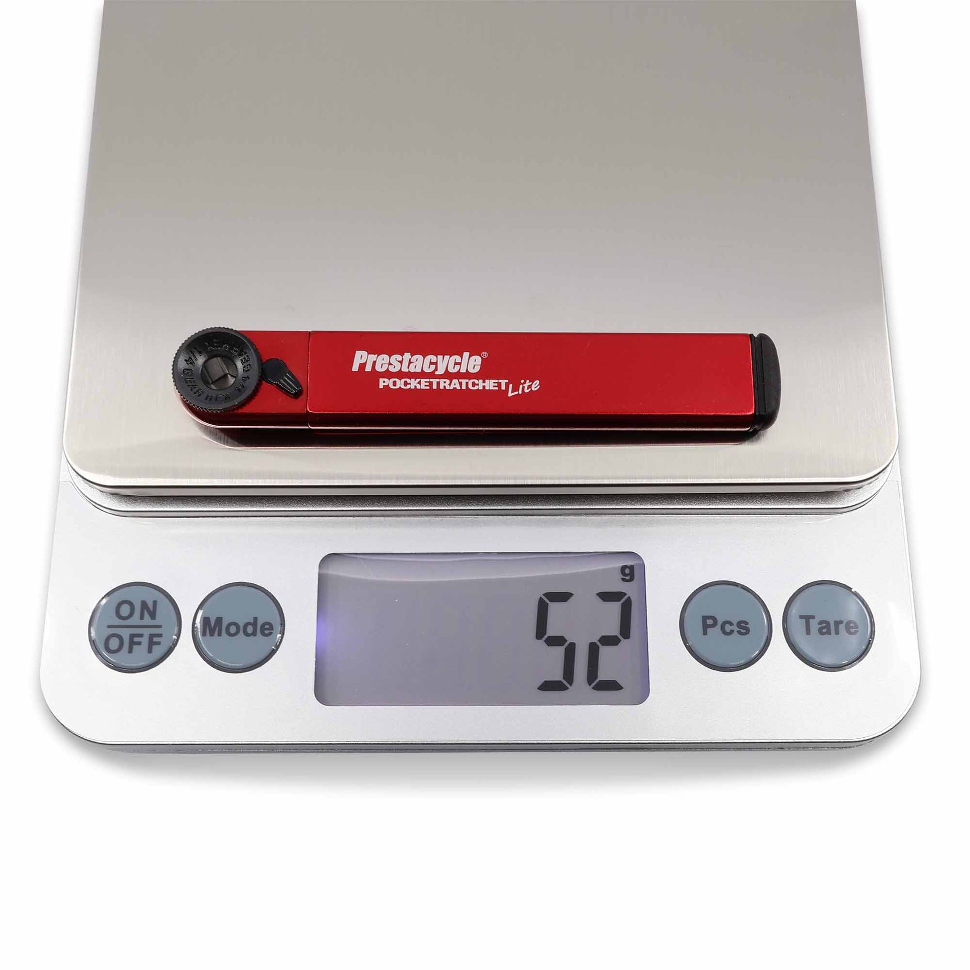 A Prestacycle PocketRatchet Lite multi-tool with bits stored in the handle rests on a digital scale reading 52 grams. The scale shows ON/OFF, Mode, Pcs, and Tare buttons.