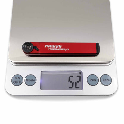 A Prestacycle PocketRatchet Lite multi-tool with bits stored in the handle rests on a digital scale reading 52 grams. The scale shows ON/OFF, Mode, Pcs, and Tare buttons.