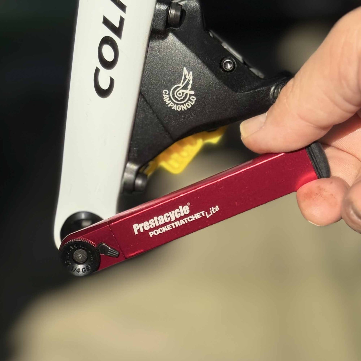 A hand uses a Prestacycle PocketRatchet Lite pocket multi-tool with bits stored in the handle to adjust a bolt on a black and white Colnago bike with Campagnolo components.