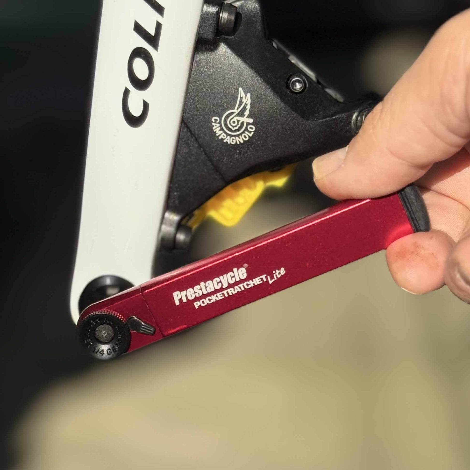 A hand uses a Prestacycle PocketRatchet Lite pocket multi-tool with bits stored in the handle to adjust a bolt on a black and white Colnago bike with Campagnolo components.