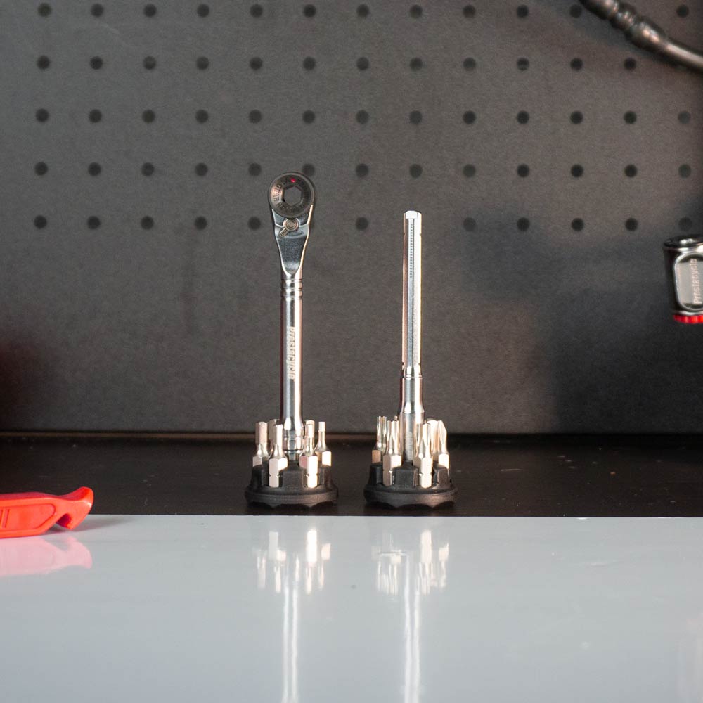 Two Prestacycle Pro T-Handle Kits by Prestacycle stand upright on a black work surface in front of a pegboard. The left kit includes a T-Handle Ratchet; the right kit features a socket extension. A red tool is partially visible on the left.