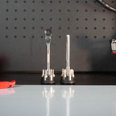 Two Prestacycle Pro T-Handle Kits by Prestacycle stand upright on a black work surface in front of a pegboard. The left kit includes a T-Handle Ratchet; the right kit features a socket extension. A red tool is partially visible on the left.