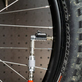 A close-up shows a bicycle tire with BIG ROLLER on the sidewall being inflated using the Prestacycle Pro Schrader Head pump from Prestacycle, featuring an auto-lock mechanism securely attached to the valve stem for optimal tire pressure.